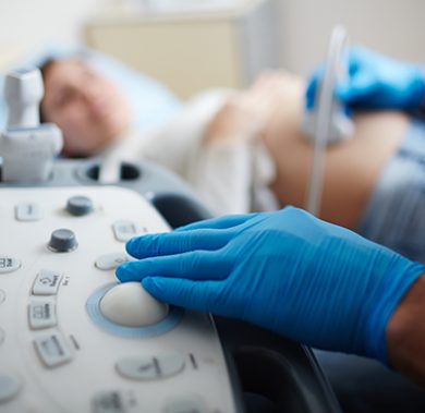 Hand of doctor in glove pressing button on panel of ultrasound equipment during regular check-up of pregnant woman