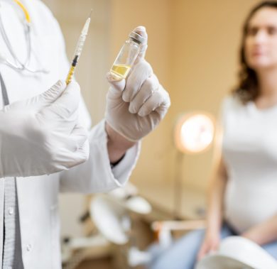 Doctor holding vaccine or some medication in the syringe, preparing for injection for a pregnant woman during a medical procedure in the clinic, close-up view