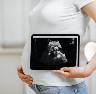 Pregnant woman holding digital tablet with an ultrasound scan of her unborn baby, standing in medical office, close-up view