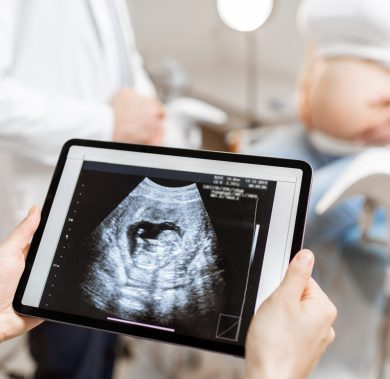 Medics with an ultrasound scan of unborn child on a digital tablet during an examination with a pregnant woman in the office, cropped view without faces