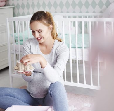 Pregnant woman with baby shoes in baby room