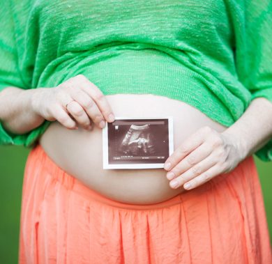 Close-up shot of a pregnant woman holding ultrasound scan in front of her bare belly. Happiness of pregnancy